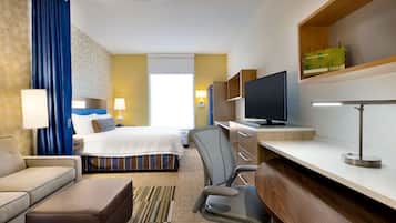 A hotel room with a bed, a desk, a chair, a TV, and a shelf with a book.