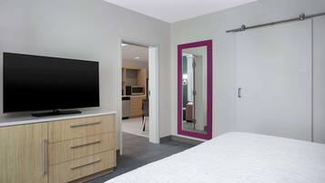 Une chambre d’hôtel moderne avec un téléviseur à écran plat posé sur une commode en bois, un grand lit et une porte dotée d’un cadre rose.