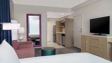 Quarto de hotel com uma cama, escrivaninha, cadeira, televisão, micro-ondas e uma pequena copa.