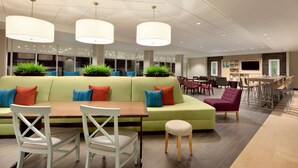 Un espace repas moderne avec un canapé vert, des chaises blanches et une table en bois. Des plantes en pot et des luminaires suspendus se trouvent au-dessus de la table.