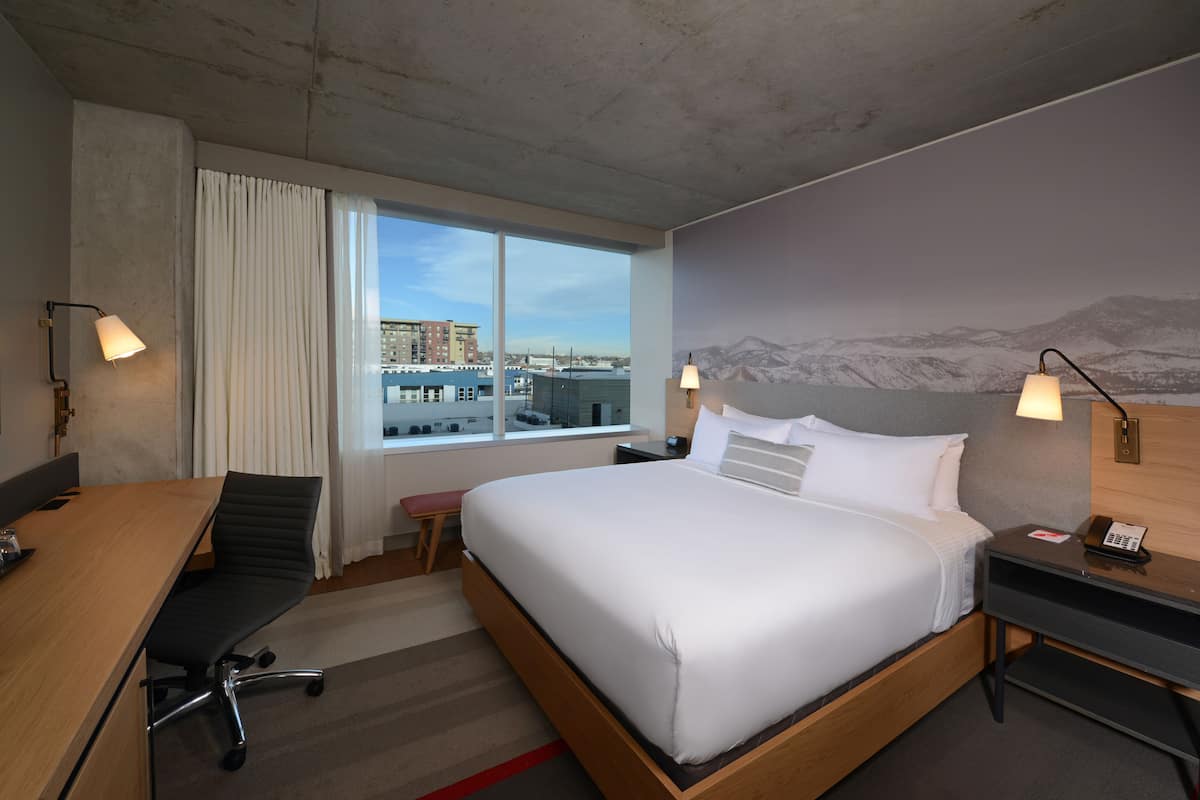 A hotel room with a large bed, a desk, and a chair. There are two lamps on either side of the bed.