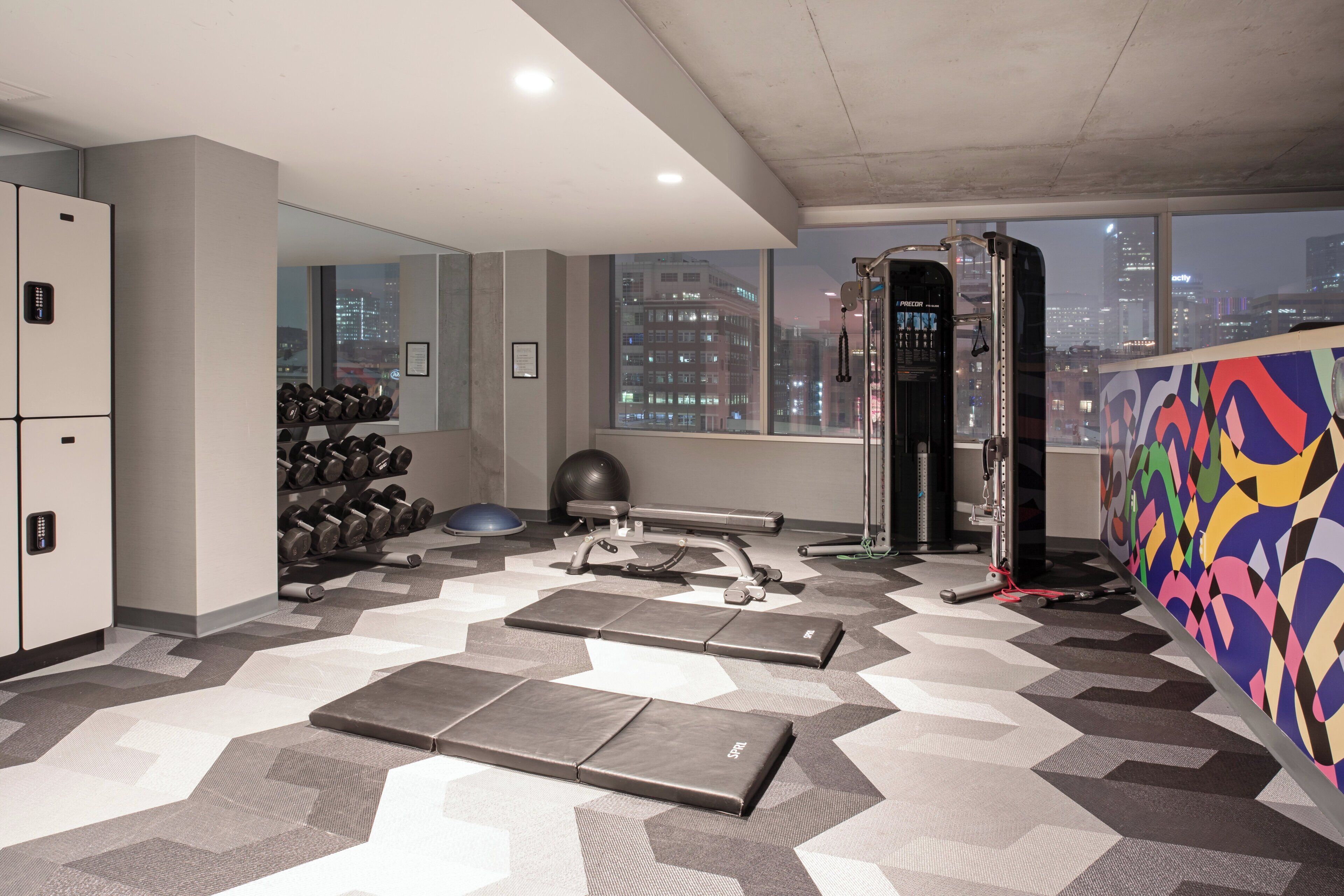 A gym with exercise equipment, a mirrored wall, and a city view.