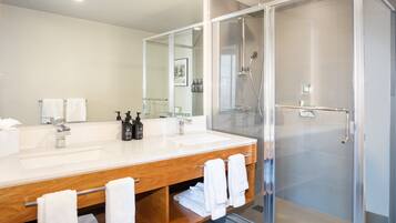 A modern bathroom with a large mirror, two sinks, a shower enclosure, and a wooden vanity with towels.