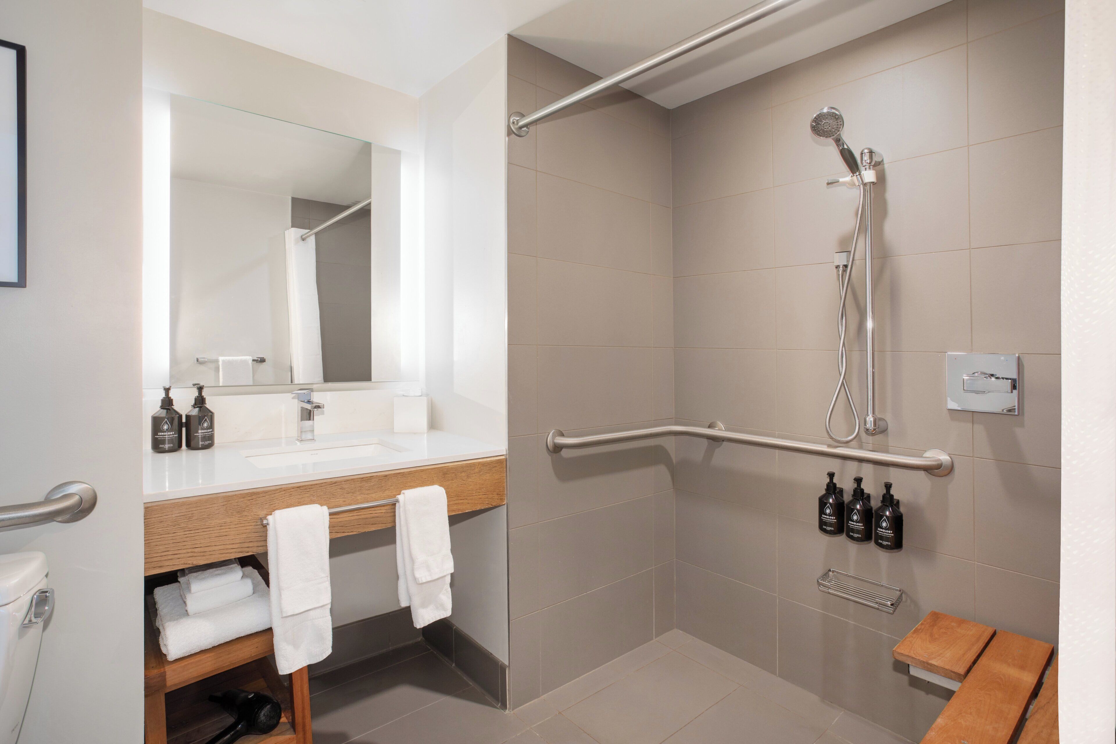 A modern bathroom with a shower, a sink with a mirror, and a wooden bench.