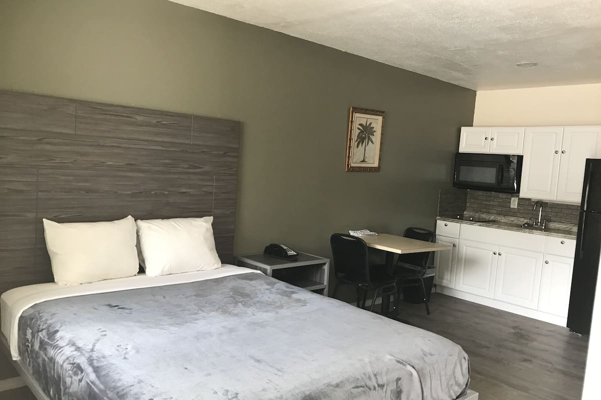 A hotel room with a bed, a desk, a chair, a microwave, and a refrigerator.
