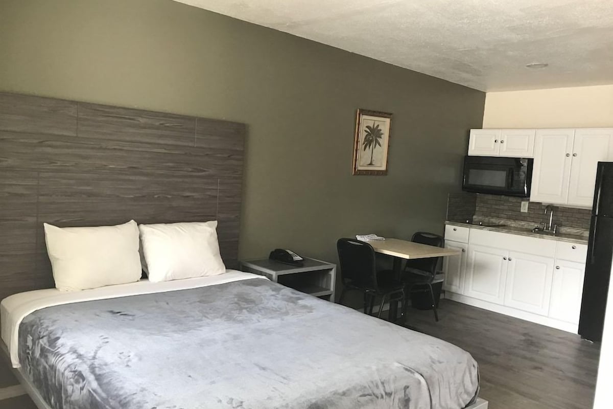 A bedroom with a bed, a desk, and a kitchenette.