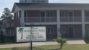 Ein zweistöckiges Gebäude mit einem Schild, das Paris Extended Stay Suites bewirbt und täglich sowie wöchentliche Preise anbietet.