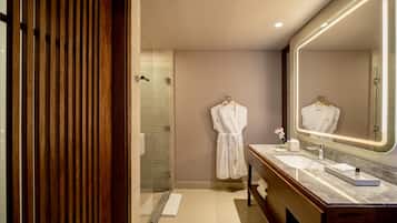 A modern bathroom with a wooden panel wall, a glass shower enclosure, a vanity with a large mirror, and a robe hanging on the wall.