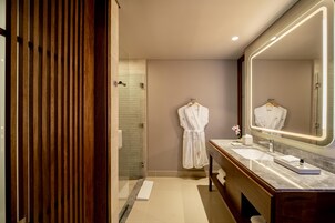 Un baño moderno con pared de paneles de madera, cabina de ducha con mampara de vidrio, tocador con un espejo grande y una bata colgada en la pared.