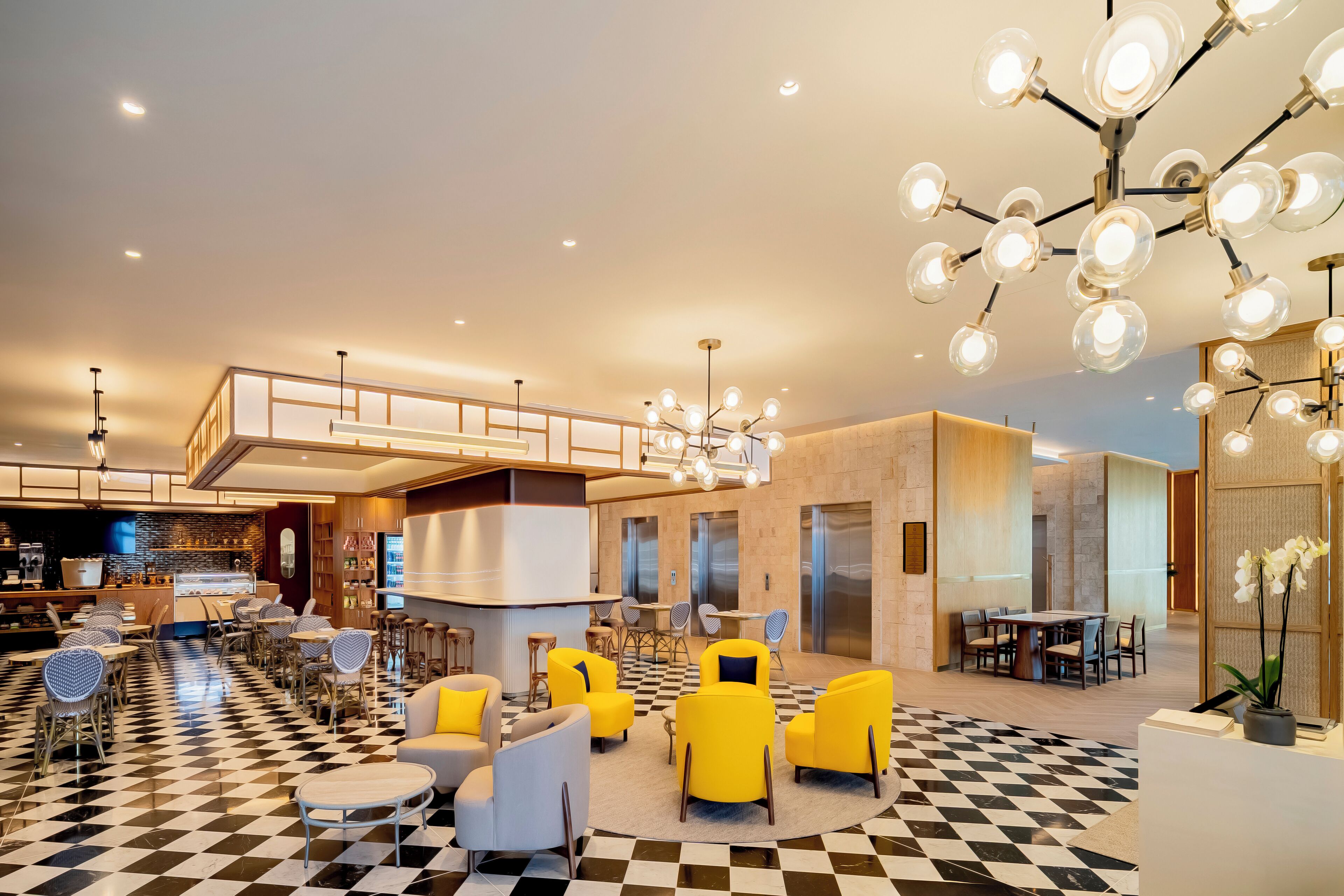 A modern hotel lobby with checkered flooring, yellow armchairs, a central seating area, and a bar.