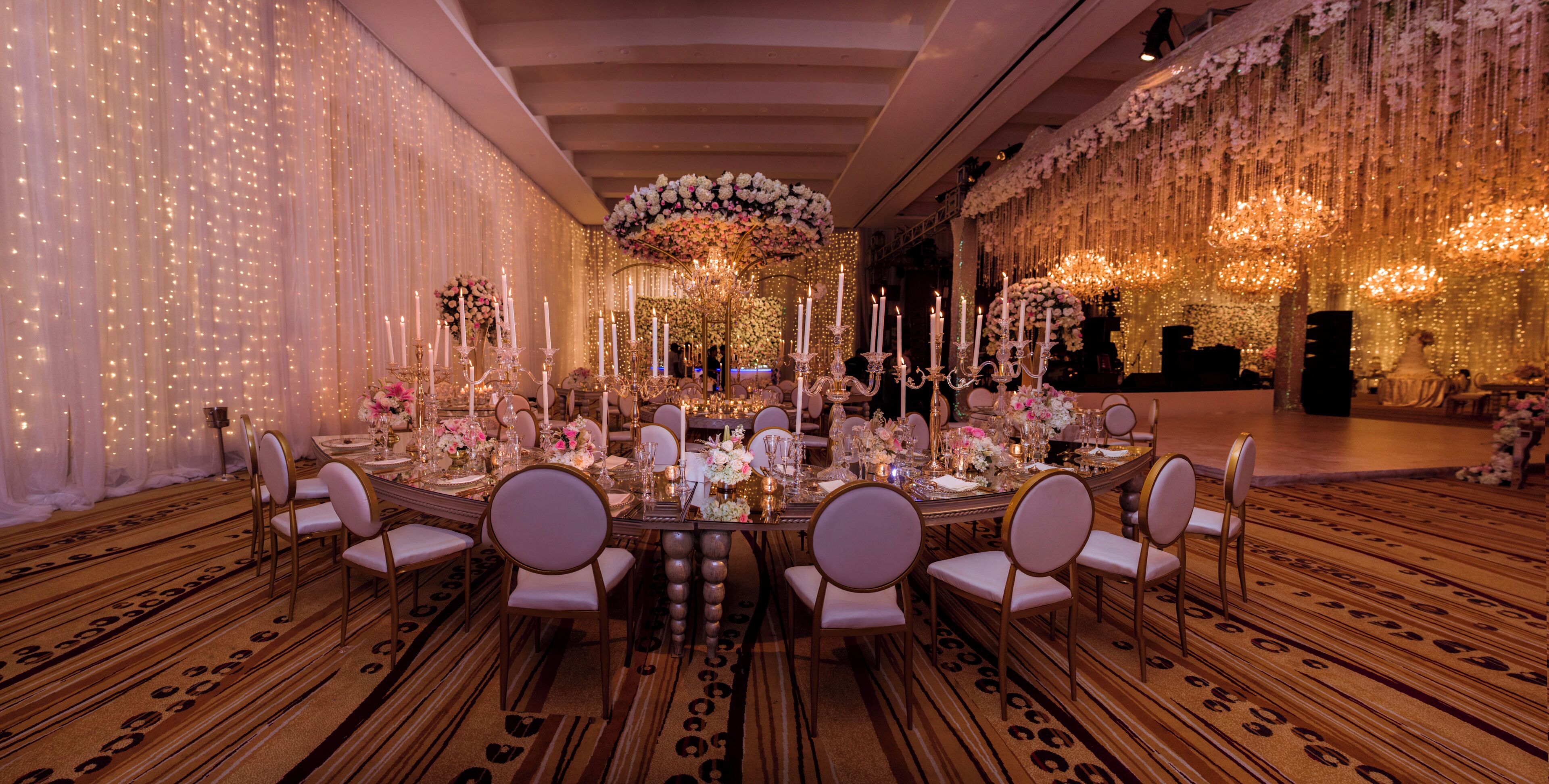 Uma sala de banquetes com uma longa mesa posta para um evento formal, rodeada de cadeiras.