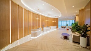 A modern lobby with wooden paneling, reception desks, a central seating area, and large windows.
