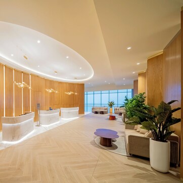 A modern lobby with wooden paneling, reception desks, a central seating area, and large windows.