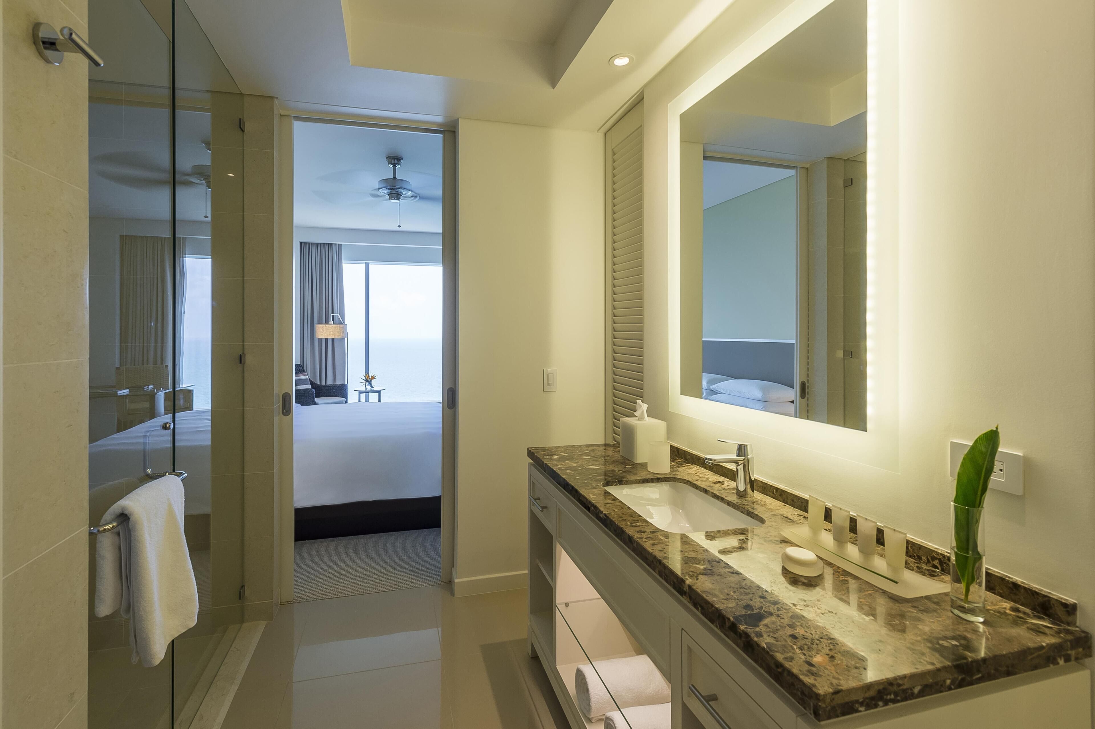 A modern bathroom with a large mirror, granite countertop, and a glass shower enclosure.