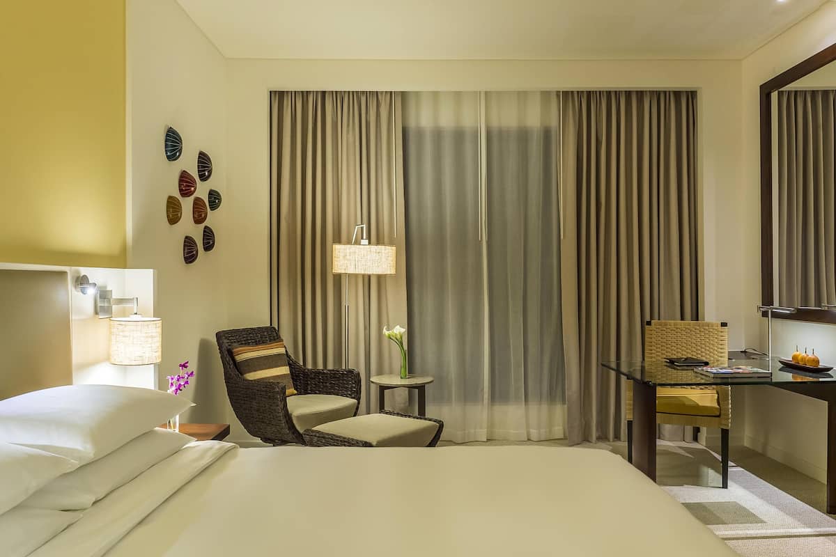 A hotel room with a bed, a chair, a small table, a lamp, and curtains.