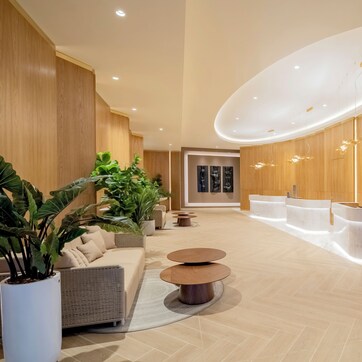 A modern lobby with a reception desk, seating area, and potted plants.
