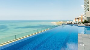 A swimming pool with a clear view of the ocean and a beach in the background.