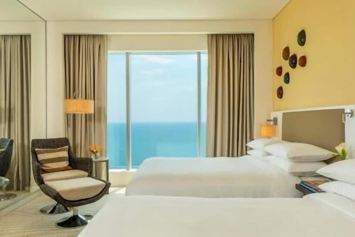 A hotel room with a bed, a chair, a lamp, and a view of the ocean.