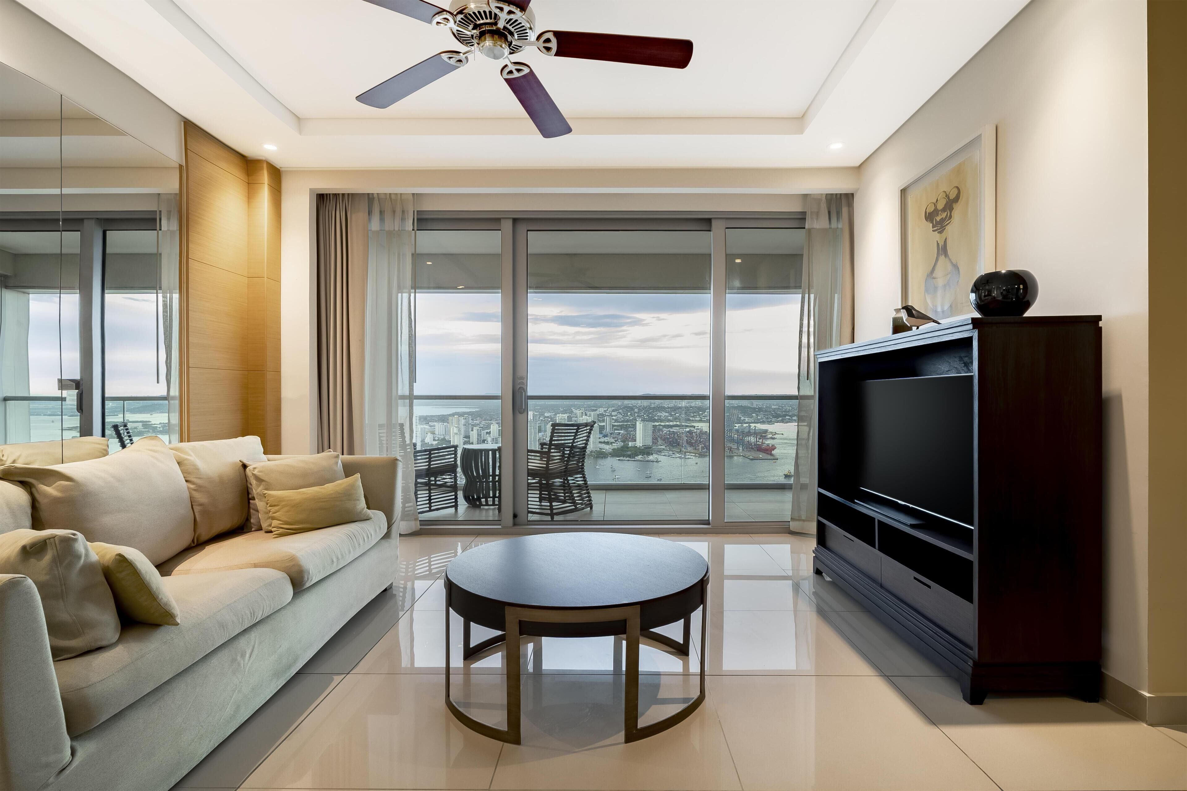 Una sala de estar moderna con un sofá, una mesa redonda, un mueble para televisión y un balcón con vistas a la ciudad.