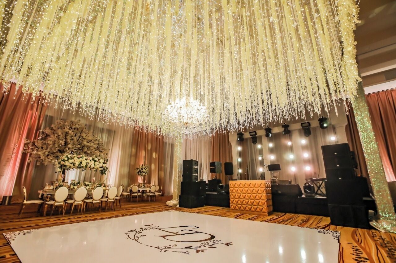 A decorated event space with a dance floor, floral arrangements, and a stage with lighting equipment.