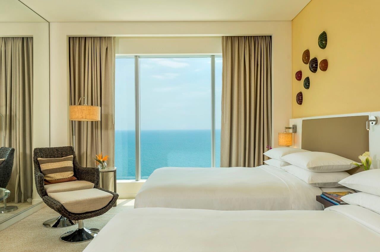 A hotel room with a large bed, a chair, a lamp, and a view of the ocean.