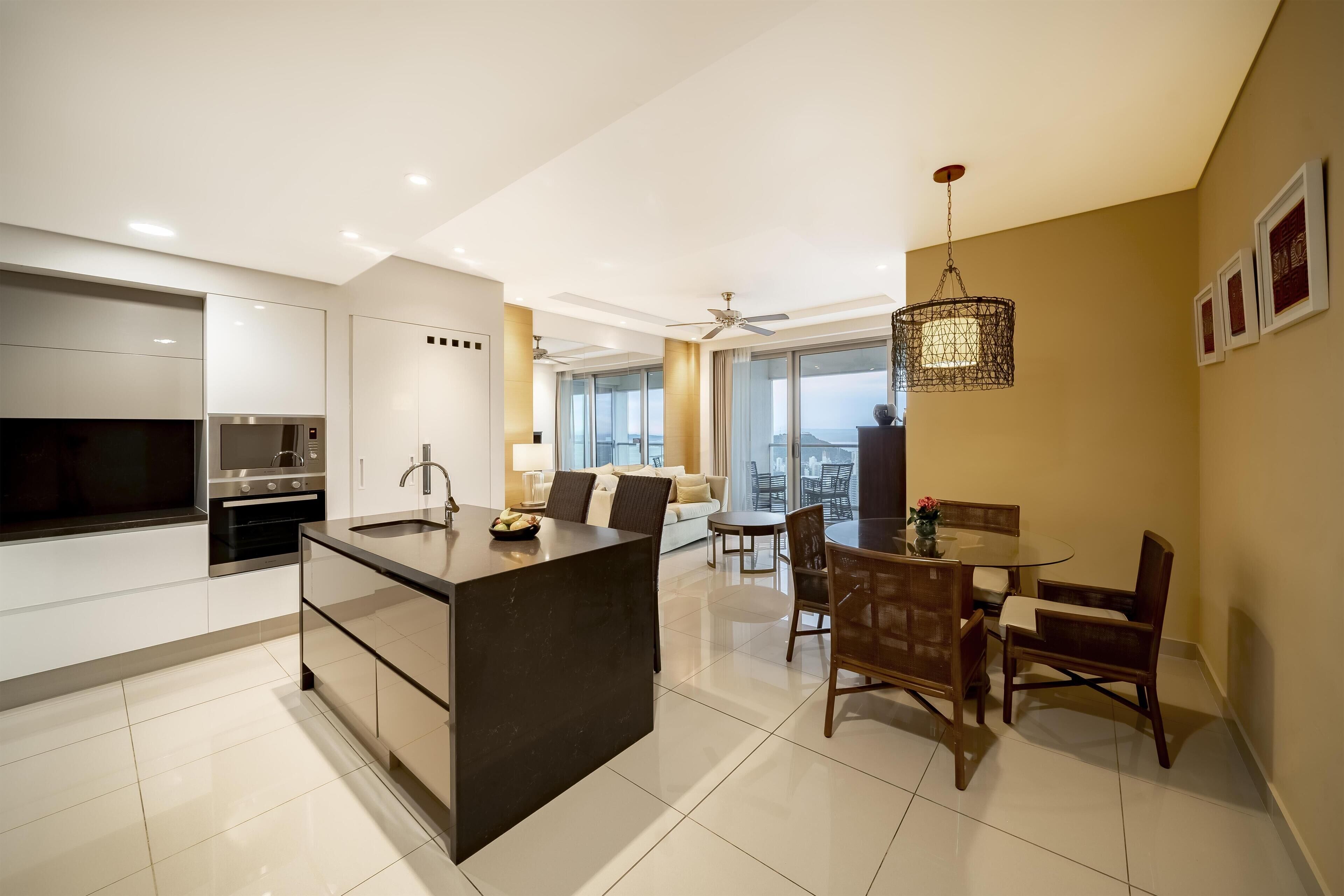 Uma cozinha moderna com uma ilha central, uma área de jantar com mesa e cadeiras redondas, e uma janela grande com vista para a cidade.