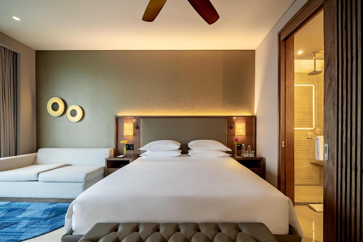 A modern hotel room with a large bed, a sofa, and a bathroom visible through an open door.