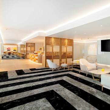 A modern hotel lobby with a central seating area, a reception desk, and a large TV screen.