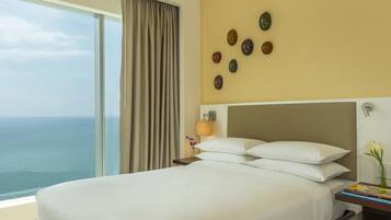 Habitación de hotel con una cama grande, una mesita de noche, una lámpara y vista al océano.