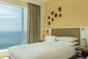 Habitación de hotel con una cama grande, una mesita de noche, una lámpara y vista al océano.