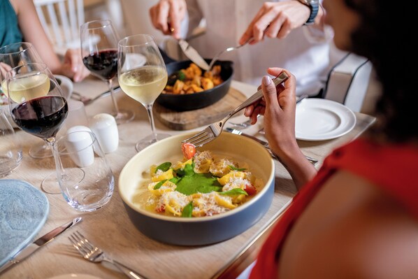 A dining table with a bowl of food, wine glasses, and cutlery.