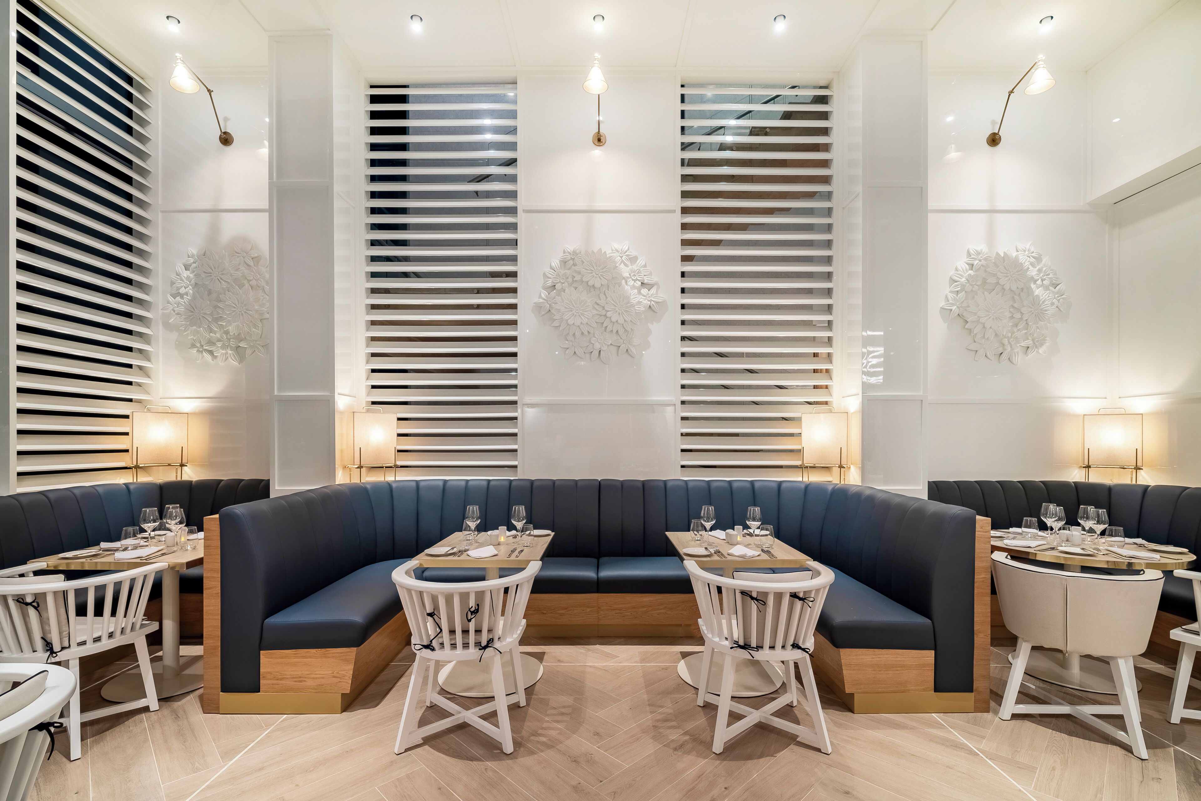 A modern restaurant with dark blue booths, white chairs, and round tables.