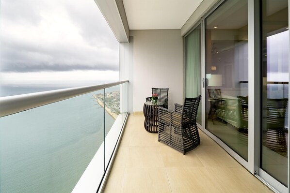 A balcony with a view of the sea, a glass door, and a seating area with a table and chairs.