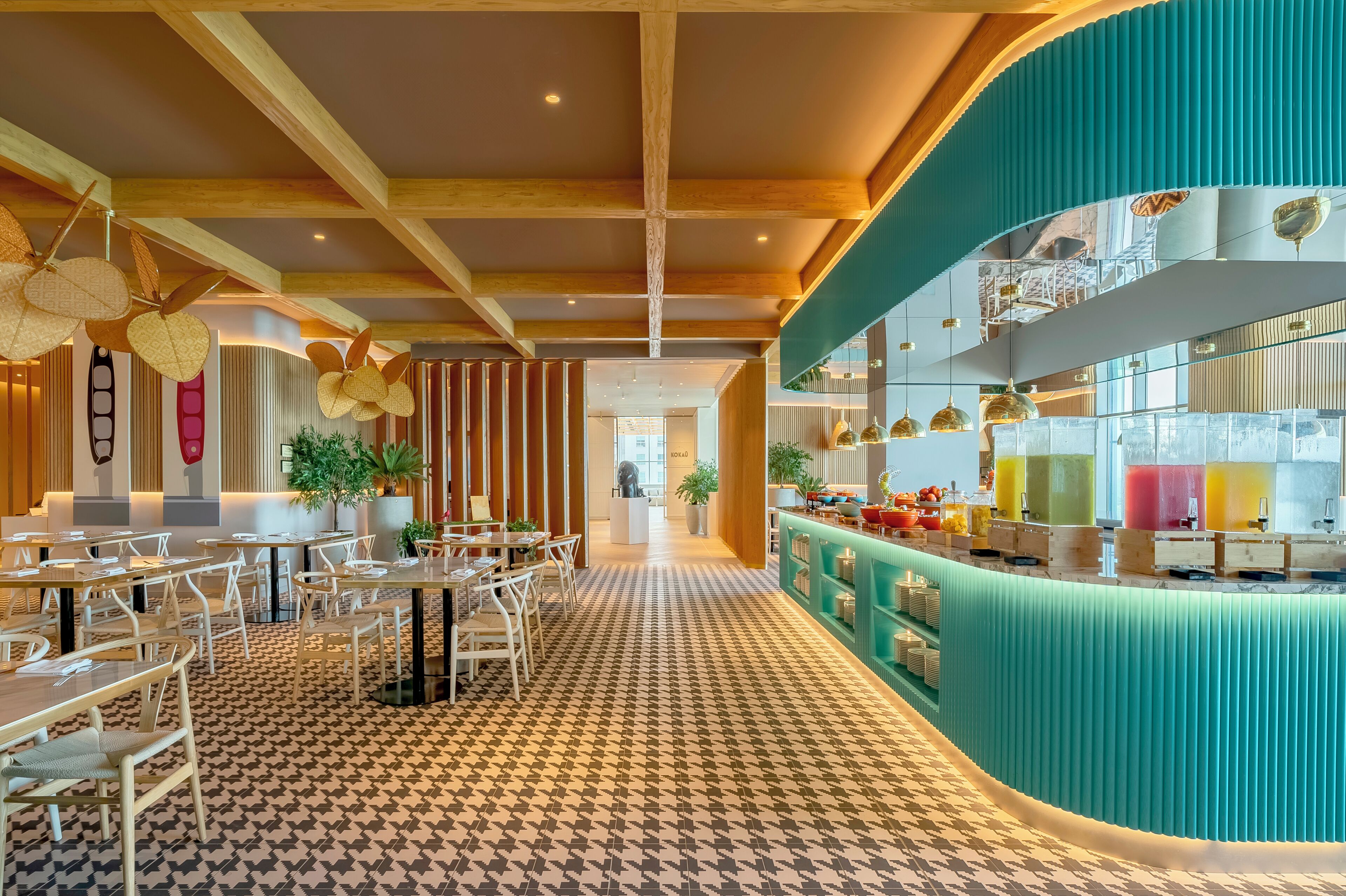 Un restaurante moderno con piso estampado, vigas de madera en el techo y una barra color turquesa con exhibición de bebidas.