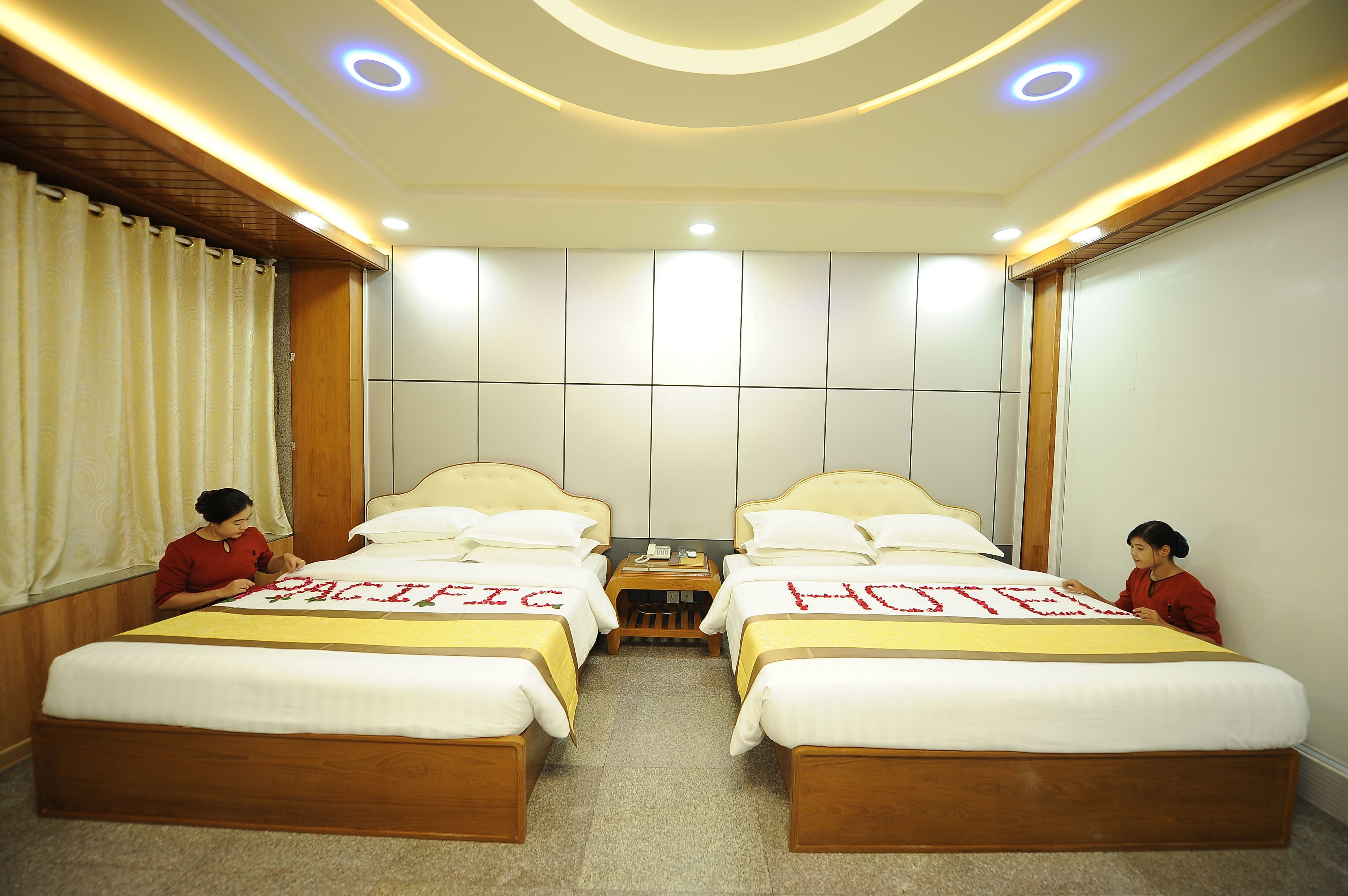 Habitación de hotel con dos camas, cada una con un cartel que dice 'PACIFIC HOTEL', cabeceros de madera y una pequeña mesa entre las camas.
