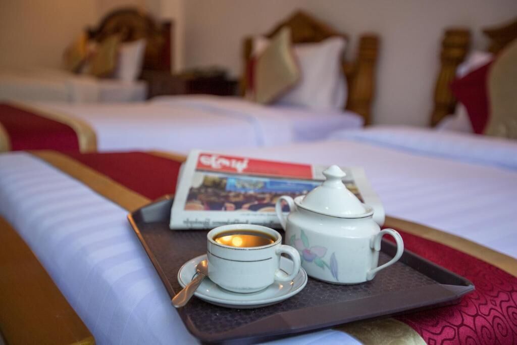 Una bandeja con una taza de café, una tetera y una revista sobre una cama.