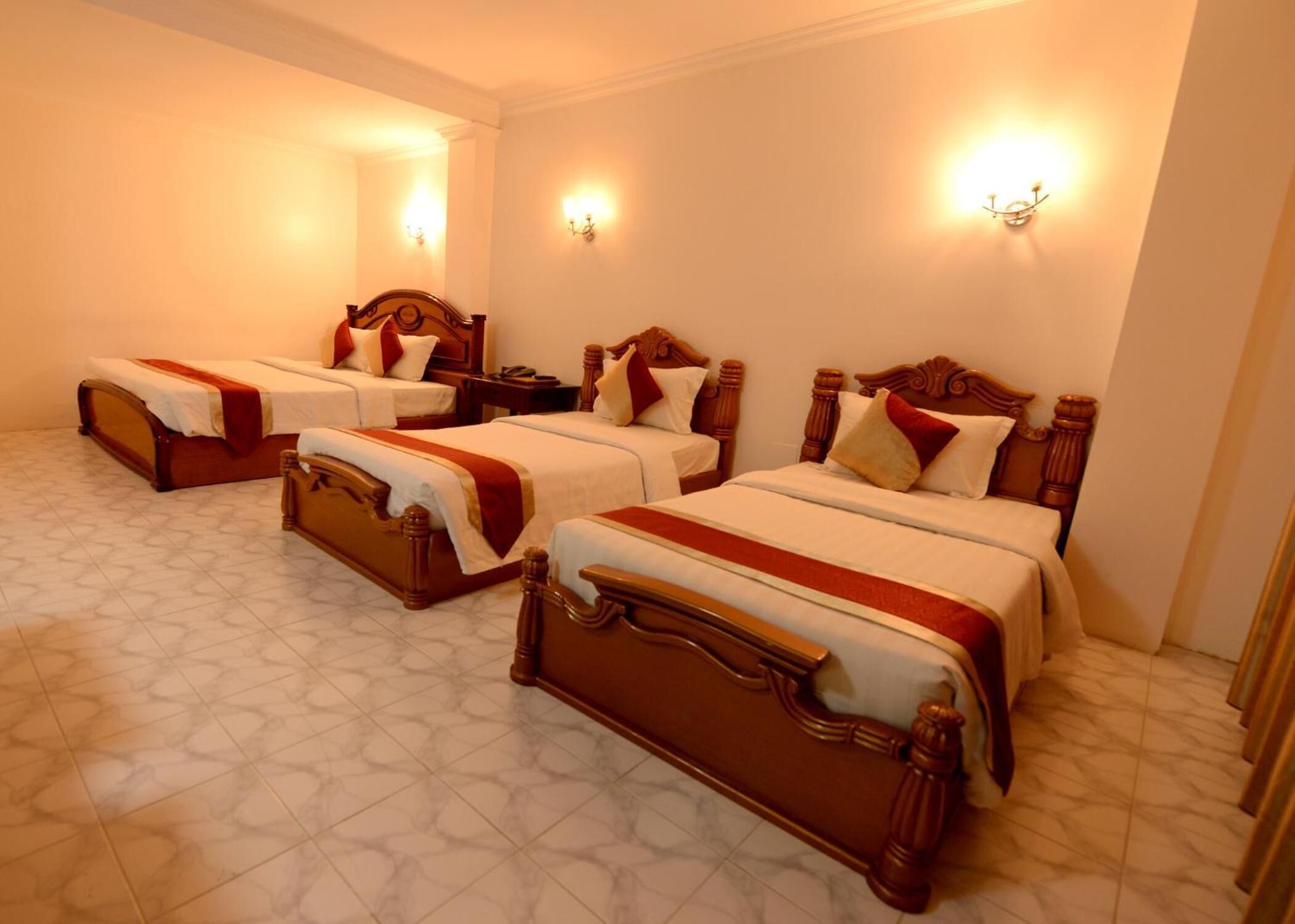 Habitación de hotel con cuatro camas, cada una con cabeceros de madera y ropa de cama blanca. Hay apliques de pared que proporcionan iluminación ambiental.