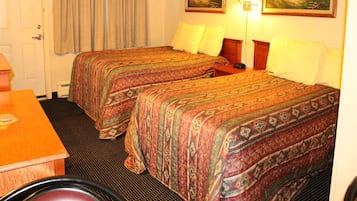 A hotel room with two beds, a desk, a chair, and two paintings on the wall.