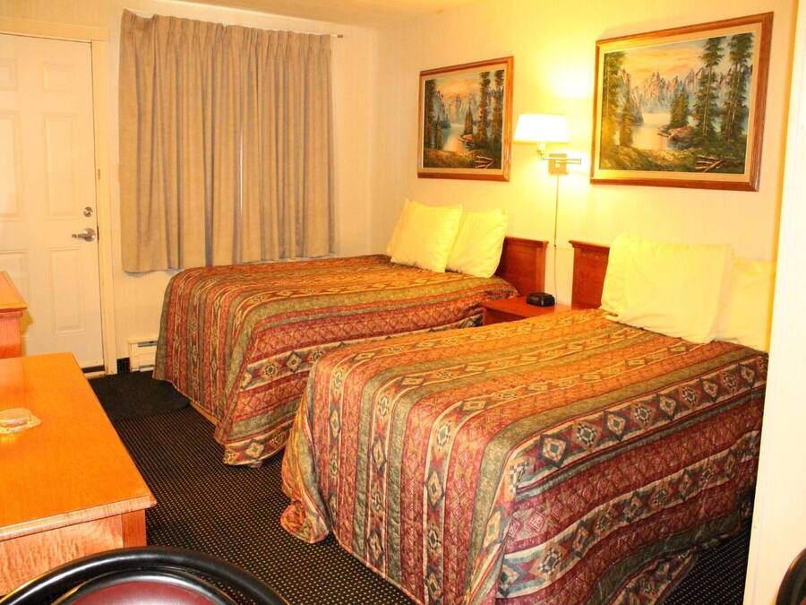 A hotel room with two beds, a desk, a chair, and two paintings on the wall.