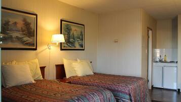 Ein Hotelzimmer mit zwei Betten, einem Nachttisch, einer Lampe, einem Gemälde und einer Küchenzeile.