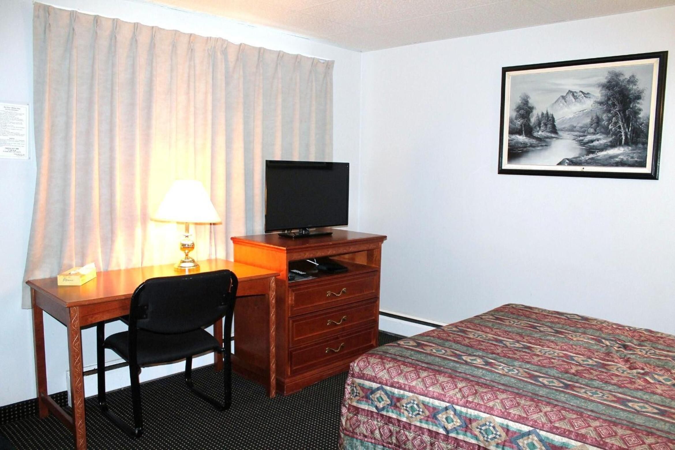 Una camera d'albergo con una scrivania, una sedia, un televisore, un comò e un letto con copriletto decorato.