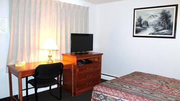 Una camera d'albergo con una scrivania, una sedia, un televisore, un comò e un letto con copriletto decorato.