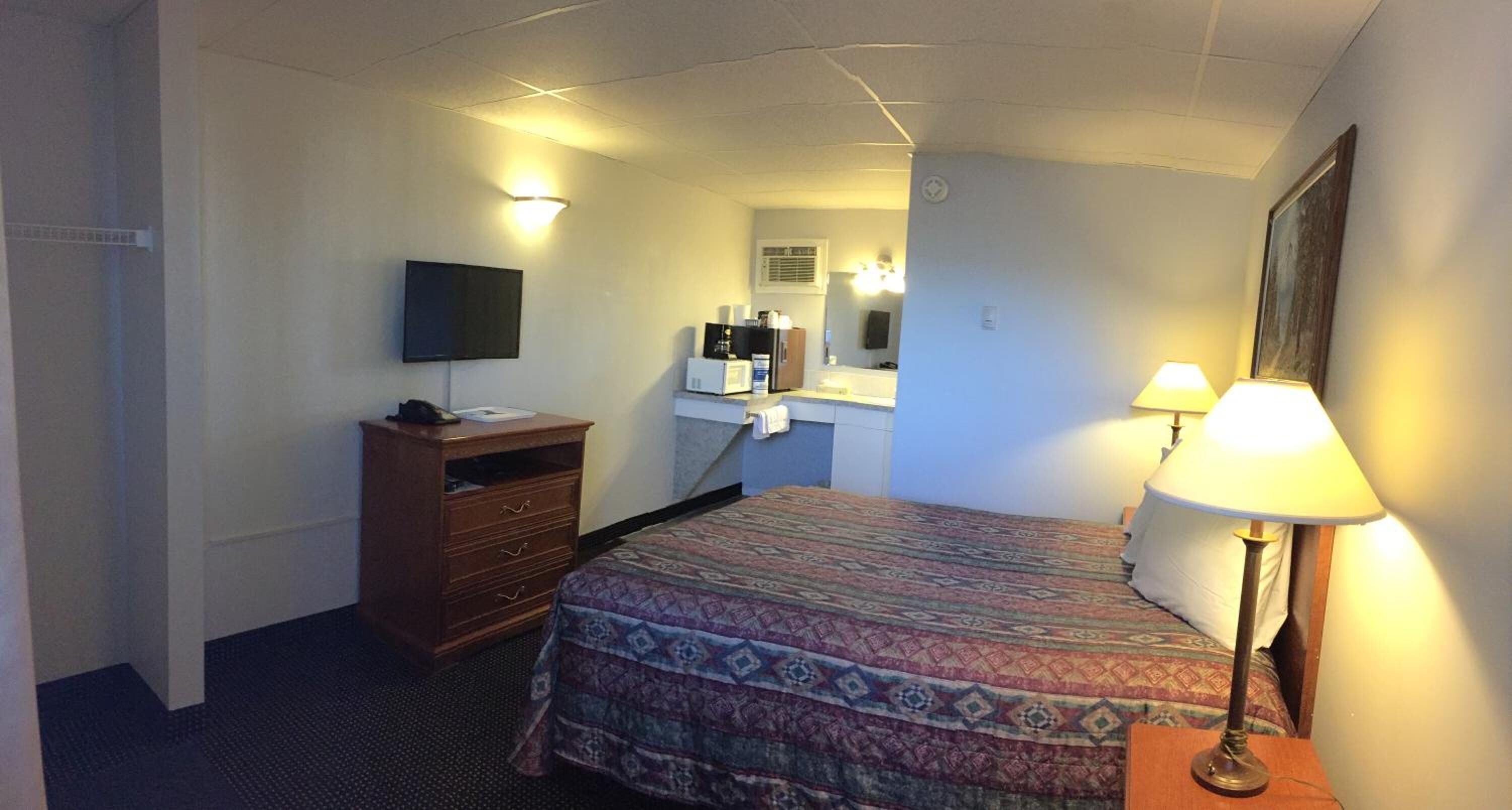 Een hotelkamer met een bed, een dressoir, een televisie, een spiegel en een lamp.