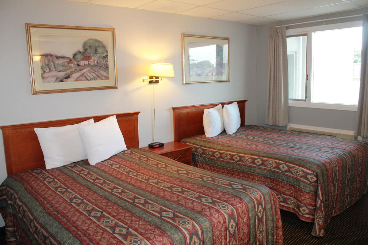 Une chambre d’hôtel avec deux lits, une table de chevet, une lampe et deux tableaux encadrés au mur.
