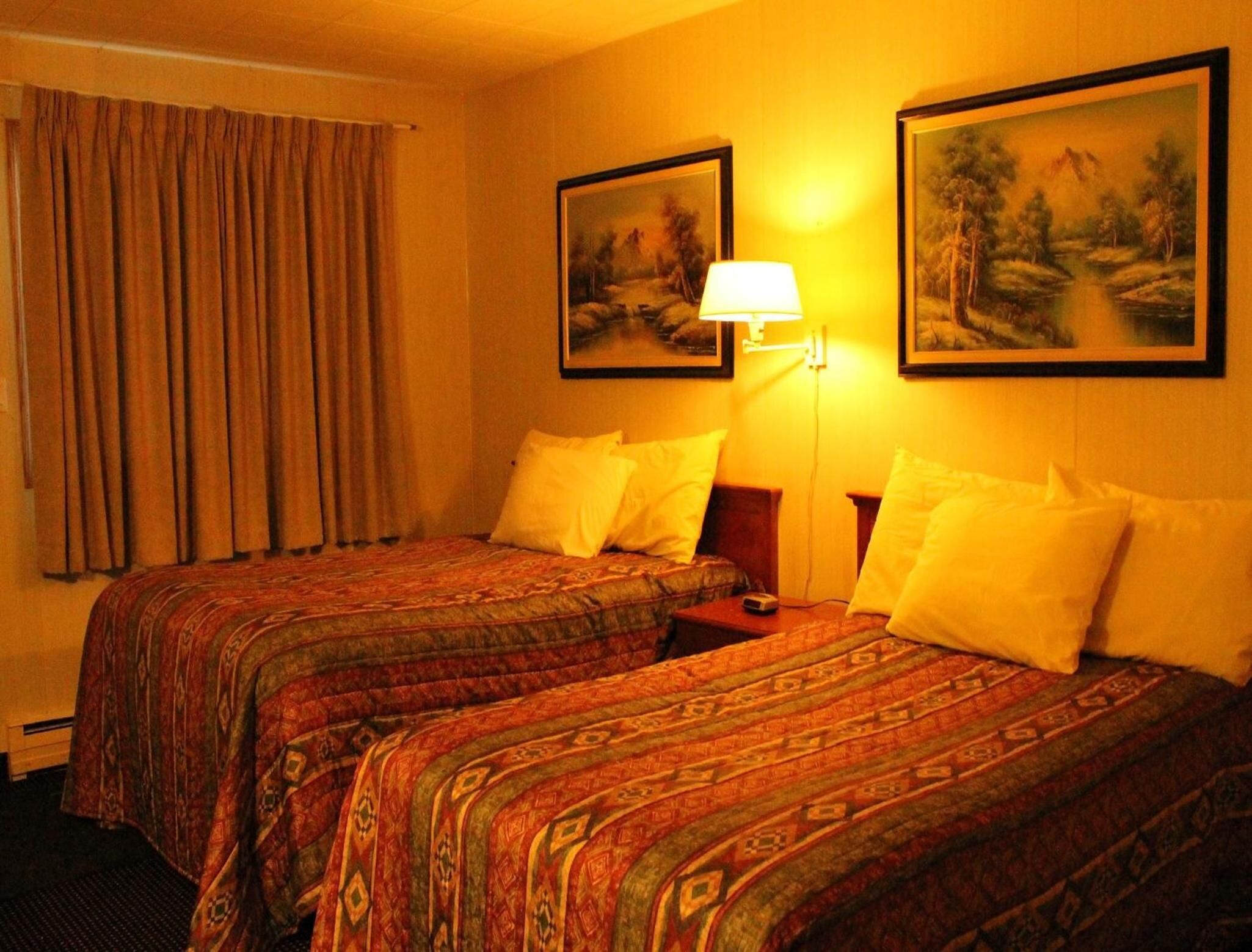 Une chambre d’hôtel avec deux lits, une lampe et deux tableaux au mur.