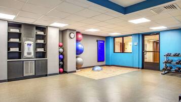 Ein Fitnessraum mit Trainingsgeräten, einer Uhr und einer Wand mit blauen Akzenten.
