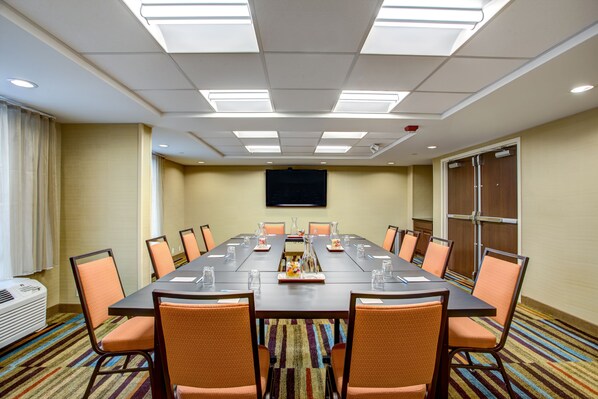 A conference room with a long table, chairs, and a flat-screen TV on the wall.
