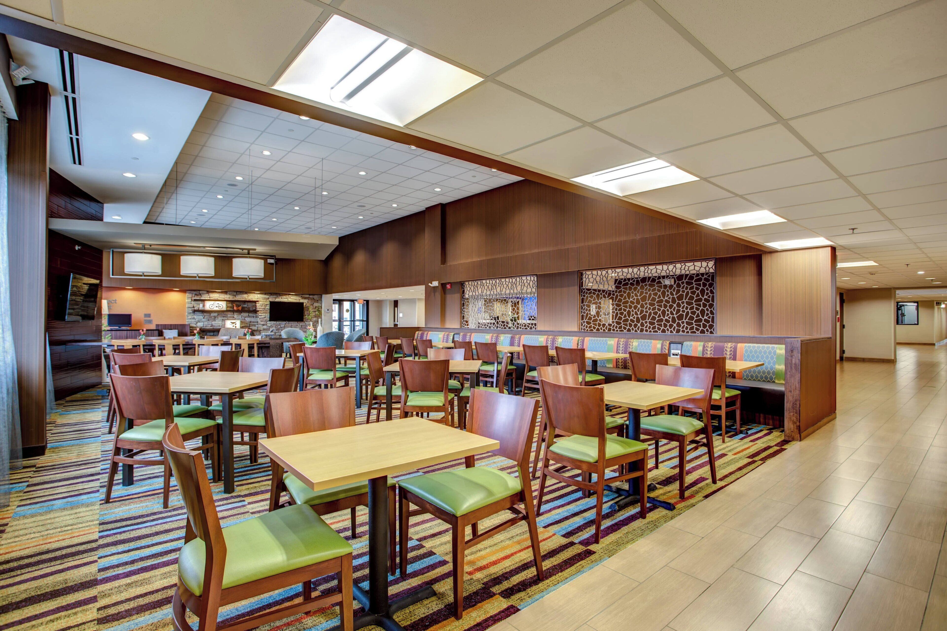 A spacious dining area with multiple tables and chairs, a central seating area with a patterned wall, and a kitchen in the background.