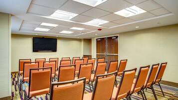 Ein Konferenzraum mit Reihen orangefarbener Stühle, einer Projektionsleinwand und einem Teppichboden.