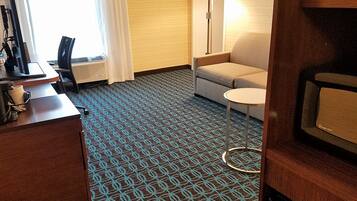 A hotel room with a patterned carpet, a desk with a lamp, a sofa, and a small round table.